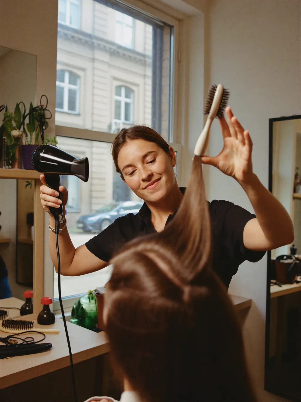Friseurin föhnt einer Kundin die Haare und führt dabei eine Rundbürste
